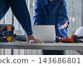 A construction site: A worker's hands as he conducts a meeting on his computer. 143686801