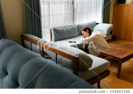 一位女士沮喪地坐在客廳的沙發上。 一位女士沮喪地坐在客廳的沙發上。 143687290