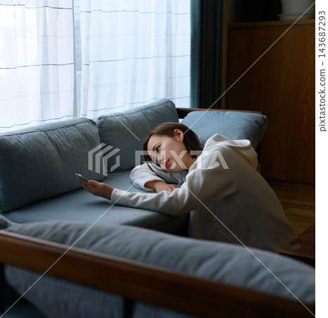 A sad woman looking downcast while looking at her smartphone A sad woman looking downcast while looking at her smartphone 143687293