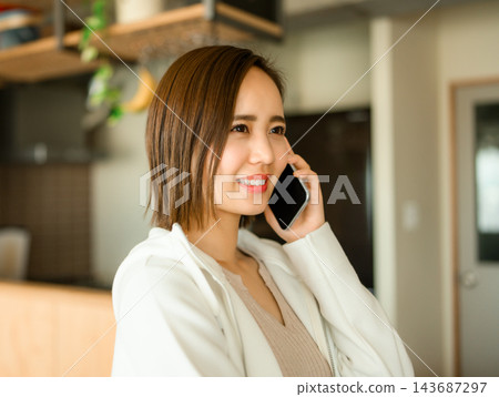 一位年輕女子一邊用智慧型手機通話一邊微笑。 一位年輕女子一邊用智慧型手機通話一邊微笑。 143687297