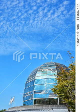 在晴朗的秋日天空和雲朵的襯托下,一座現代化的玻璃穹頂建築高聳入雲。 在晴朗的秋日天空和雲朵的襯托下,一座現代化的玻璃穹頂建築高聳入雲。 143687386
