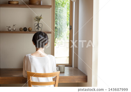 一位看起來像是自由工作者的日本女性，在她明亮時尚的家中，倚窗使用筆記型電腦工作。 143687999