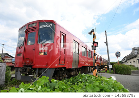 一列紅色火車沿著鐵路線飛馳而過，藍天白雲，綠樹成蔭。 143688792