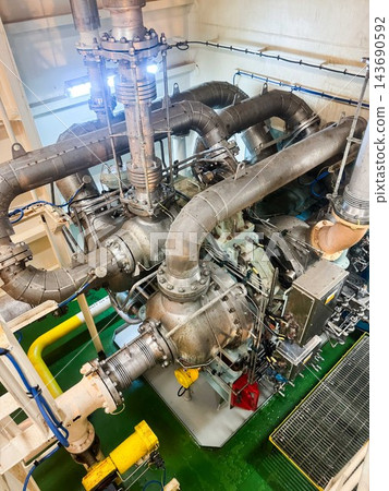 High angle view of a powerful marine turbocharger system with heavy insulated pipelines inside vessel engine room. High angle view of a powerful marine turbocharger system with heavy insulated pipelines inside vessel engine room. 143690592