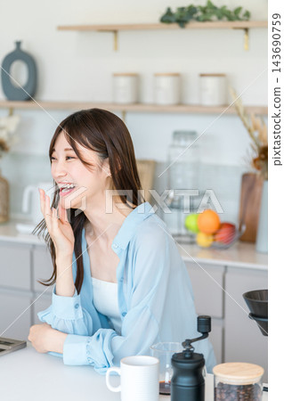 一位年輕女子在廚房裡笑容滿面，手摀著嘴。享受咖啡的愜意生活。 143690759