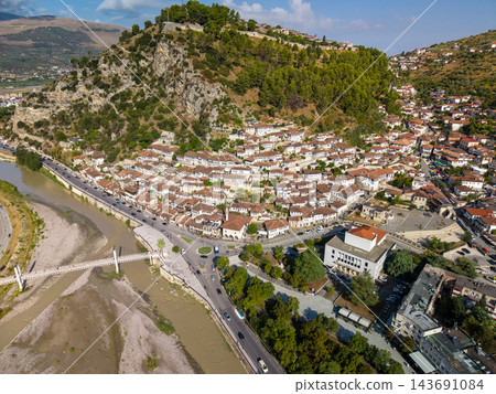 Berat Albania rises along green hillside above river, its traditional white houses and terracotta roofs packed together. Elevated town panorama reveals historic architecture and surrounding mountains. Berat Albania rises along green hillside above river, its traditional white houses and terracotta roofs packed together. Elevated town panorama reveals historic architecture and surrounding mountains. 143691084