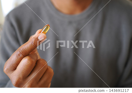 Individual grasping a yellow capsule in their hand while inside a building 143691217