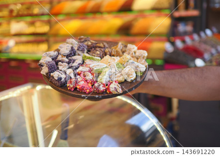A person holds a plate of turkish delights in a shop filled with colorful treats A person holds a plate of turkish delights in a shop filled with colorful treats 143691220