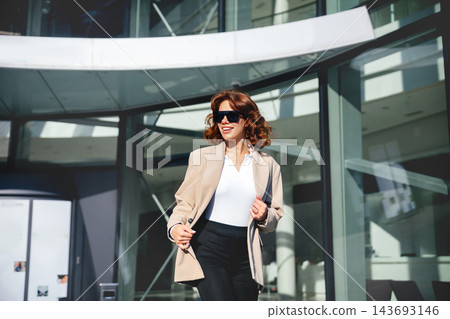 Beauty woman walking confidently with stylish blazer and sunglasses. Beautiful woman enjoying professional lifestyle near modern office entrance. Business elegance concept. Beauty woman walking confidently with stylish blazer and sunglasses. Beautiful woman enjoying professional lifestyle near modern office entrance. Business elegance concept. 143693146