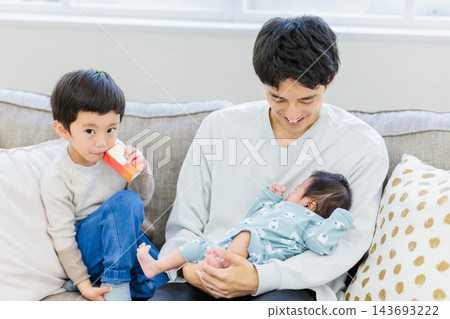 一對父子坐在沙發上，父親抱著嬰兒。 143693222