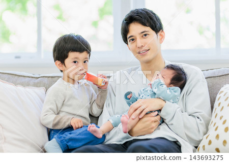 一對父子坐在沙發上，父親抱著嬰兒。 143693275