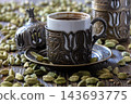 Traditional coffee cup with ornate design surrounded by cardamom pods 143693775