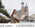 Pretty young woman staying on the street holding paper map in hands. 30s girl in hat posing on Market Square in Krakow. Traveling Europe, High quality photo, Vacation concept 143694884