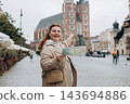 Pretty young woman staying on the street holding paper map in hands. 30s girl in hat posing on Market Square in Krakow. Traveling Europe, High quality photo, Vacation concept 143694886