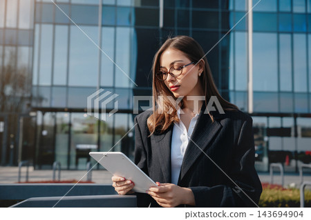 Beautiful Business Woman Reading Documents Outside Modern Office Building Wearing Black Blazer And Glasses. Corporate Lifestyle Concept Female Professional Urban Architecture 143694904