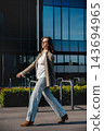 Attractive Woman Walking In City Wearing Beige Blazer And Jeans Near Modern Office Building. Casual Business Lifestyle Concept Female Urban Style 143694965