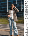Attractive Woman Walking Near Office Building Wearing Beige Blazer And Jeans Talking On Smartphone. Casual Business Lifestyle Concept Female Urban 143694970