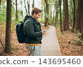 A man in a forest is looking for a way using a mobile navigator - to get lost in the forest. Male explorer looking for connection to the internet or using gps navigator app on phone 143695460