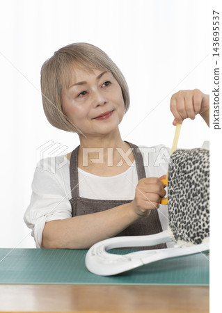 一位老婦人在客廳裡改造了一個娃娃椅,作為她的DIY愛好。 一位老婦人在客廳裡改造了一個娃娃椅,作為她的DIY愛好。 143695537