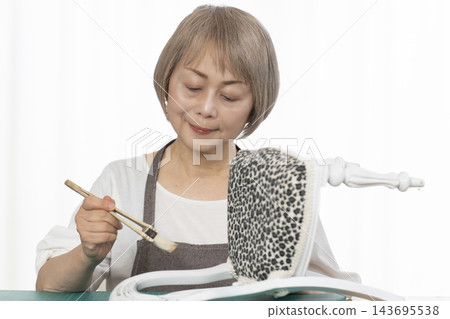 一位老婦人在客廳裡改造了一個娃娃椅,作為她的DIY愛好。 一位老婦人在客廳裡改造了一個娃娃椅,作為她的DIY愛好。 143695538