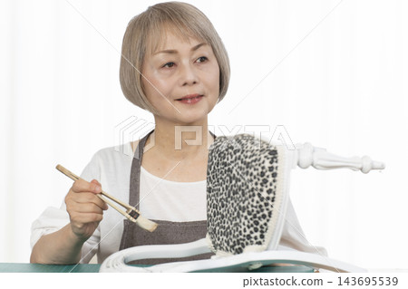 一位老婦人在客廳裡改造了一個娃娃椅,作為她的DIY愛好。 一位老婦人在客廳裡改造了一個娃娃椅,作為她的DIY愛好。 143695539