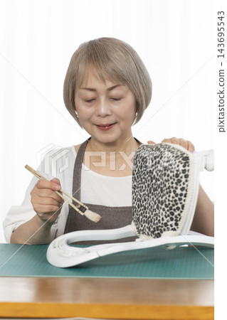 一位老婦人在客廳裡改造了一個娃娃椅,作為她的DIY愛好。 一位老婦人在客廳裡改造了一個娃娃椅,作為她的DIY愛好。 143695543