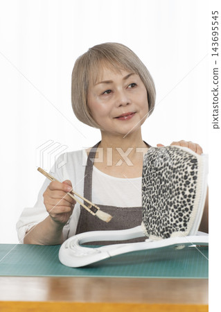 一位老婦人在客廳裡改造了一個娃娃椅,作為她的DIY愛好。 一位老婦人在客廳裡改造了一個娃娃椅,作為她的DIY愛好。 143695545
