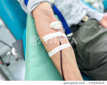 Blood donation process. Man sits in special chair while medical staff collect blood from his vein. Represents volunteering, saving lives, and supporting blood banks Blood donation process. Man sits in special chair while medical staff collect blood from his vein. Represents volunteering, saving lives, and supporting blood banks 143695824