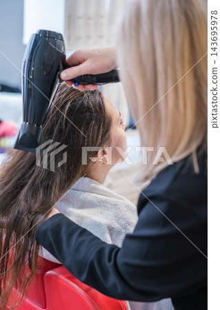 The beauty salon setting highlights a hairdresser, long hair, blow drying, a hair dryer, a female client, and a keratin treatment The beauty salon setting highlights a hairdresser, long hair, blow drying, a hair dryer, a female client, and a keratin treatment 143695978