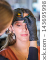 A beauty salon appointment centers on eyebrow lamination, eyebrow shaping, a young woman, eyebrow tinting, brow styling, and a beautician 143695998