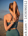 Rear view of a fit young woman practicing yoga outdoors, stretching her arms behind her back in cow face pose with clasped hands against a clear sunny blue sky, featuring beach and gomukhasana 143696012