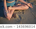 Viewed from above, the hands of a woman form Chin Mudra, the Consciousness Seal, on her knees during Padmasana yoga, Lotus Pose, while sitting on beach sand 143696014