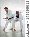 A jiu jitsu instructor controls the straight arm of his partner under his armpit during a standing waki gatame armlock drill on the tatami 143696018