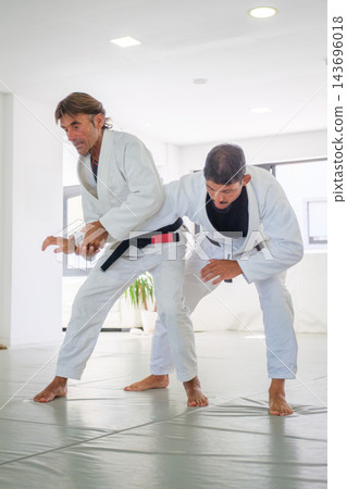 A jiu jitsu instructor controls the straight arm of his partner under his armpit during a standing waki gatame armlock drill on the tatami 143696018