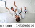 A Brazilian jiu jitsu instructor prepares a juji gatame armbar from guard, holding the arm of his partner while bringing a leg toward the head 143696019
