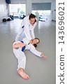 A female martial artist finishes ko-uchi-gari with an inside ankle reap, keeping a firm gi grip as her training partner lands backward on the tatami 143696021