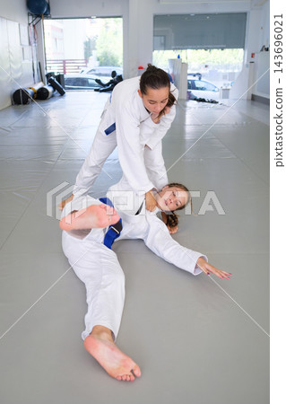 A female martial artist finishes ko-uchi-gari with an inside ankle reap, keeping a firm gi grip as her training partner lands backward on the tatami 143696021