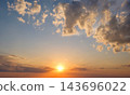 Bright sunset colors paint the sky while clouds gather in dramatic formations above the horizon, creating a peaceful evening scene. 143696022