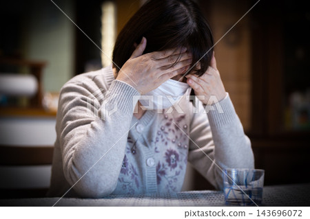 一位中老年婦女在家中客廳戴著口罩，她正在與疾病奮戰。 143696072
