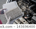 A woman compares a dirty car engine air filter with a new one. 143696400