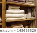 Neat stack of soft white and beige bath towels on wooden shelves in modern bathroom closet, alongside ceramic soap dispensers and bathroom accessories, creating clean and cozy home interior atmospher 143696629
