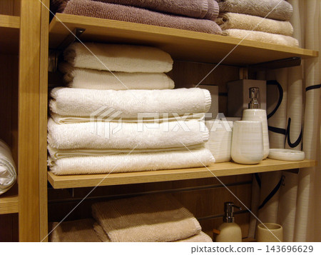 Neat stack of soft white and beige bath towels on wooden shelves in modern bathroom closet, alongside ceramic soap dispensers and bathroom accessories, creating clean and cozy home interior atmospher Neat stack of soft white and beige bath towels on wooden shelves in modern bathroom closet, alongside ceramic soap dispensers and bathroom accessories, creating clean and cozy home interior atmospher 143696629