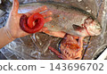 A man holds in his palm a large, intact skein of bright red roe, removed during the gutting process. Nearby, on a sheet of plastic film, lies the gutted carcass of a rainbow trout 143696702