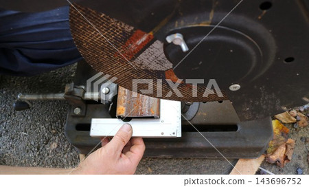 A worker places a metal square against a section of tubing held in a vise to check the angle accuracy before making a cut. The machine is equipped with a chop saw featuring a large abrasive disc. A worker places a metal square against a section of tubing held in a vise to check the angle accuracy before making a cut. The machine is equipped with a chop saw featuring a large abrasive disc. 143696752