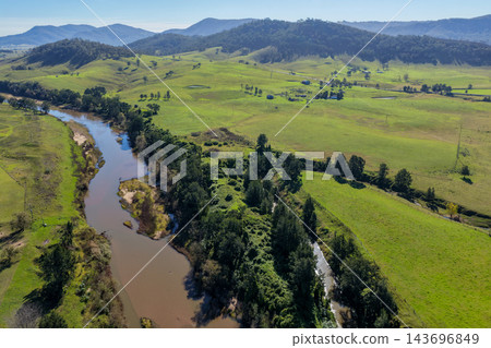 Aerial view of a winding river bordered by green farmland and wooded hills in Lambs Valley, Hunter Valley, New South Wales, Australia. 143696849