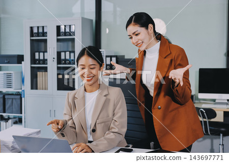 Two Asian businesswomen discussing work while walking outside a modern office building, one holding a digital tablet Two Asian businesswomen discussing work while walking outside a modern office building, one holding a digital tablet 143697771