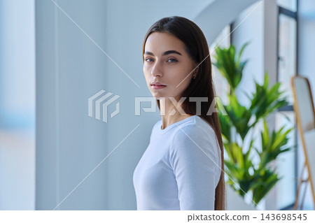 Serious young female student looking at camera in modern indoor setting Serious young female student looking at camera in modern indoor setting 143698545