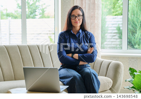 Confident businesswoman with laptop sitting on sofa at home remote office workspace Confident businesswoman with laptop sitting on sofa at home remote office workspace 143698548