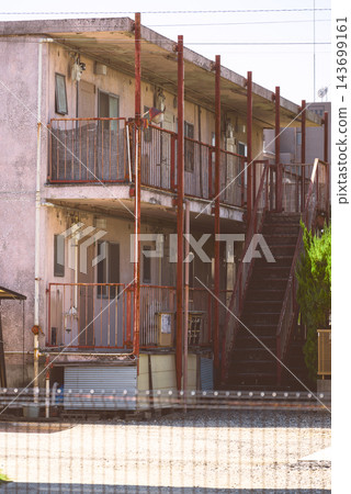 A vertically oriented photograph of the exterior of an old apartment building, showing the exterior corridor and plumbing fixtures, with rusty iron staircases and railings. A vertically oriented photograph of the exterior of an old apartment building, showing the exterior corridor and plumbing fixtures, with rusty iron staircases and railings. 143699161