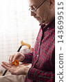 Older Man Holding Medication Bottle and Pill in Home Setting 143699515